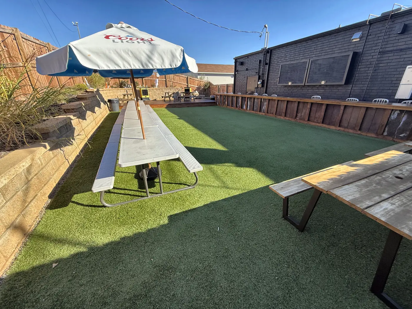 Long picnic tables under a Coors Light umbrella beside the wooden drink rail