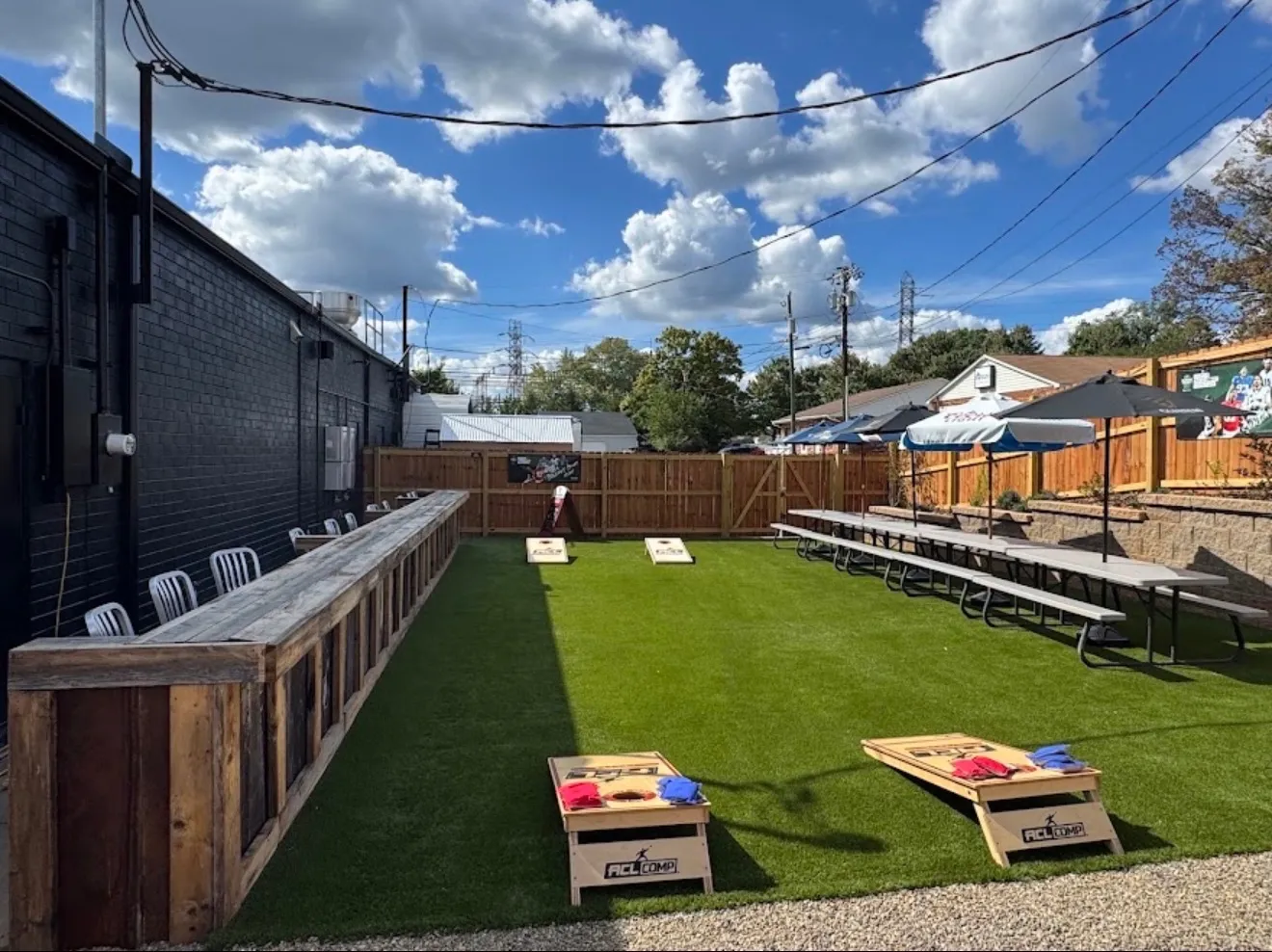 Cornhole boards on the turf, with the long wooden drink rail and picnic tables