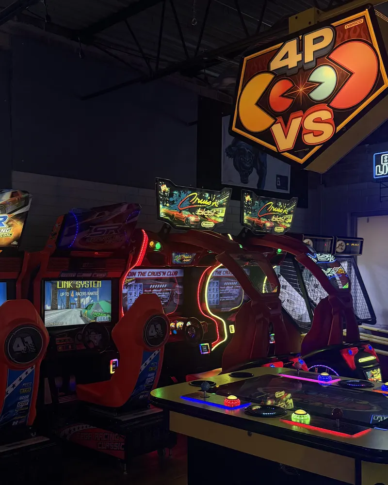 Row of sit-down racing cabinets under a 4-player Pac-Man sign